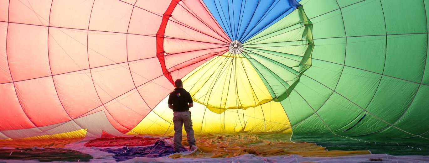 A distanced perspective of two people (a male in a manual wheelchair and a femme stood next to him) arm in arm at the top of Bank Top, Rosedale, overlooking a valley of fields and trees.